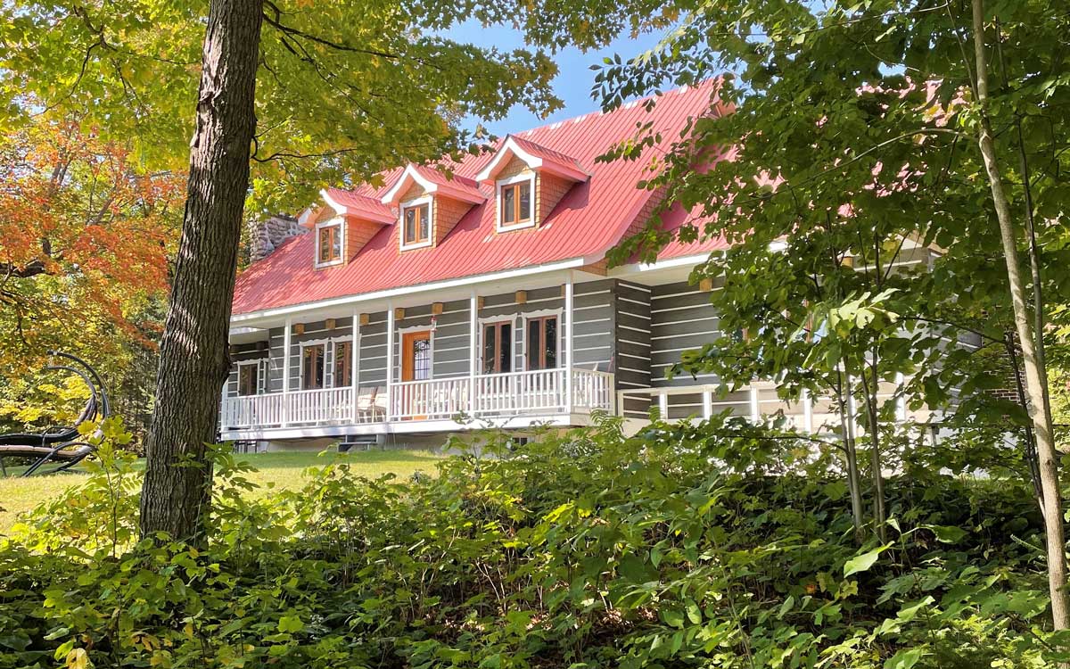 Grand chalet à toit rouge, vue d'entre du feuillage